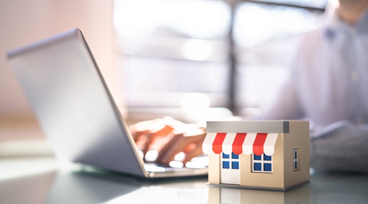 A person using a laptop behind a small cardboard box of a small building.